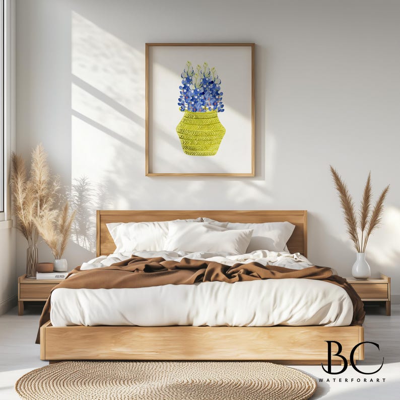 May include: A watercolor painting of a bouquet of blue flowers in a yellow woven basket. The painting is framed and hanging on a white wall in a bedroom setting.