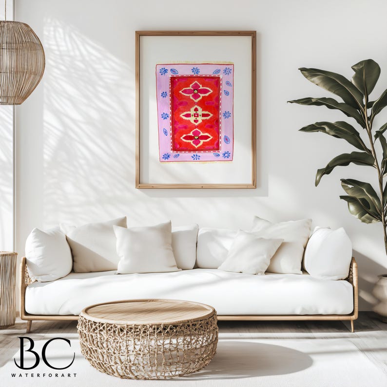 May include: A white couch with white pillows sits in front of a framed print of a red and pink rug with blue accents. A woven wicker coffee table sits in front of the couch.
