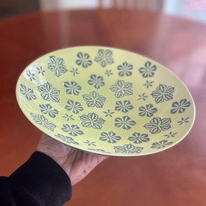 May include: A large, yellow ceramic bowl with a floral pattern in dark blue. The bowl is decorated with a repeating design of stylized flowers.