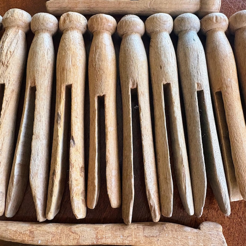 May include: A close-up of a set of wooden clothespins. The clothespins are all natural wood and have a simple design. They are arranged in a row, with the tips of the clothespins pointing towards the viewer.