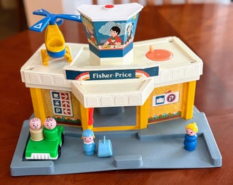 Puede incluir: Juego de juguetes Fisher-Price vintage con un edificio amarillo y blanco, un helicóptero, figuras y un coche verde. El edificio tiene un toldo azul con el logotipo de Fisher-Price e ilustraciones. El juego incluye varias figuras de plástico pequeñas.