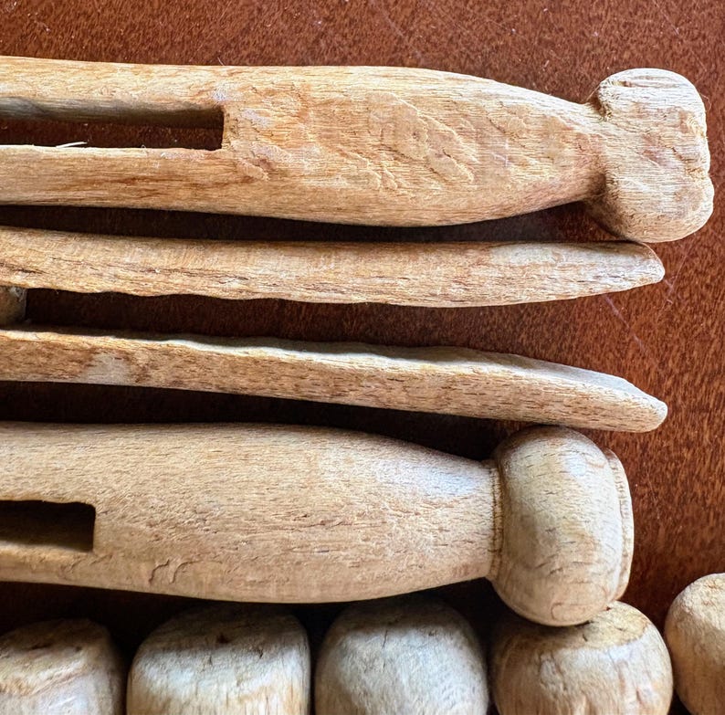 May include: Four wooden clothespins with a rounded end and a slot in the middle. The clothespins are stacked on top of each other. The clothespins are made of natural wood and have a rustic look.