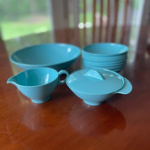 May include: A set of turquoise blue plastic kitchenware, including a large bowl, a smaller bowl with a lid, a creamer, and a set of four smaller bowls stacked together.