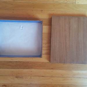 May include: A wooden box with a blue trim and a white sand interior. The lid is made of wood and is sitting next to the box.