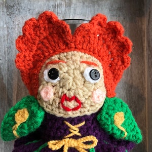 May include: Crocheted mug cozy featuring a whimsical character with red hair, a purple dress, green sleeves, and yellow accents.