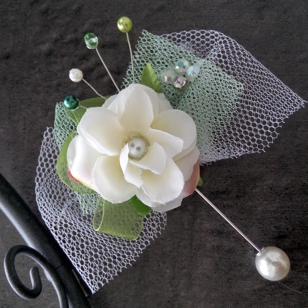 Cette épingle boule de boutonnière est en métal argenté, décorée d'une fleur de soie blanche / écru