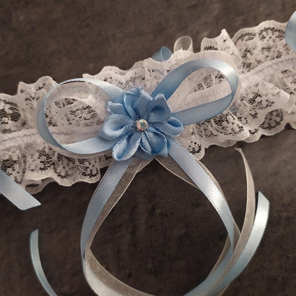 Jolie jarretière en dentelle blanche garnie d'une fleur de satin et strass et de nœuds en ruban de satin bleu clair