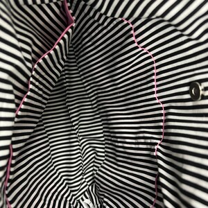 K&ouml;nnte beinhalten: Das Innere einer schwarz-wei&szlig; gestreiften Tasche mit rosa Besatz. Die Tasche hat einen einzigen Druckknopfverschluss.