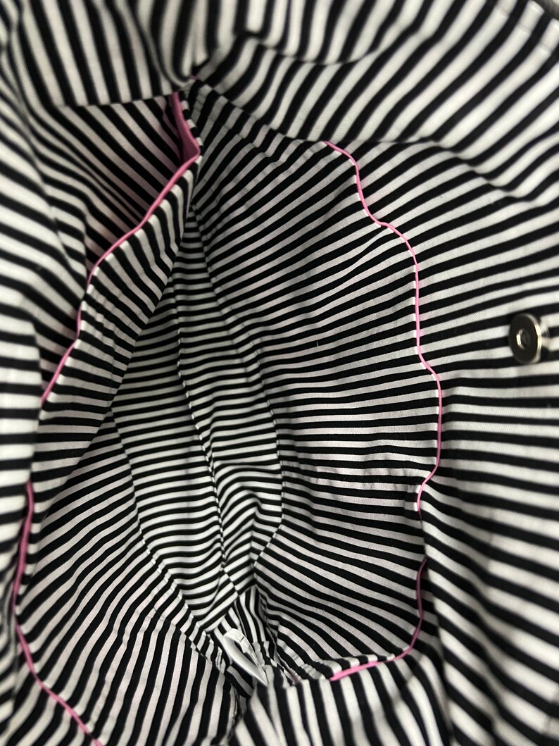 K&ouml;nnte beinhalten: Das Innere einer schwarz-wei&szlig; gestreiften Tasche mit rosa Besatz. Die Tasche hat einen einzigen Druckknopfverschluss.