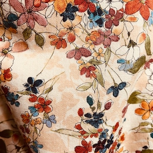 Puede incluir: Una tela beige con un patr&oacute;n floral. Las flores son en tonos de rojo, naranja, azul y rosa. La tela tiene una superficie texturizada.