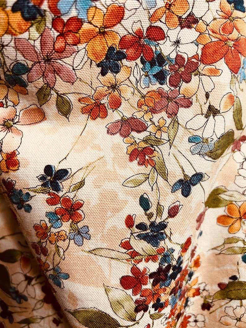 Puede incluir: Una tela beige con un patr&oacute;n floral. Las flores son en tonos de rojo, naranja, azul y rosa. La tela tiene una superficie texturizada.
