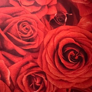 May include: Close-up of a fabric with a pattern of red roses. The roses are in various stages of bloom, with tightly furled buds and fully opened blossoms. The color palette is dominated by shades of red, with darker tones in the center of the roses.