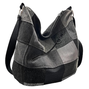 May include: A grey and black patchwork shoulder bag. The bag has a zip closure and a smaller zipped pocket. The adjustable strap is black. The bag is made from a soft, textured fabric, with a variety of grey tones.