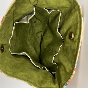 Puede incluir: El interior de una bolsa de mano de color verde y blanco con una correa marr&oacute;n. La bolsa tiene un forro verde y varios bolsillos.