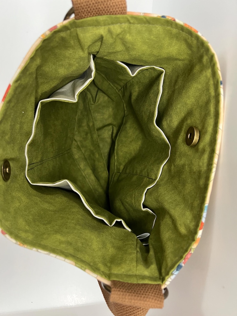 Puede incluir: El interior de una bolsa de mano de color verde y blanco con una correa marr&oacute;n. La bolsa tiene un forro verde y varios bolsillos.