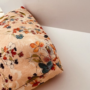 Puede incluir: Una bolsa de tela beige con estampado floral que presenta una variedad de colores, incluyendo naranja, rojo, azul y verde.