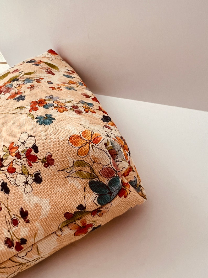 Puede incluir: Una bolsa de tela beige con estampado floral que presenta una variedad de colores, incluyendo naranja, rojo, azul y verde.