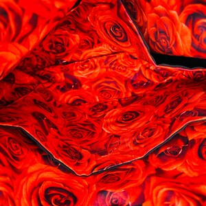 May include: Interior view of a bag with a vibrant red rose pattern. The fabric is densely covered with detailed rose blooms in varying shades of red, creating a rich and textured appearance. Black trim outlines the pockets and edges.
