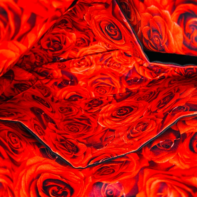 May include: Interior view of a bag with a vibrant red rose pattern. The fabric is densely covered with detailed rose blooms in varying shades of red, creating a rich and textured appearance. Black trim outlines the pockets and edges.