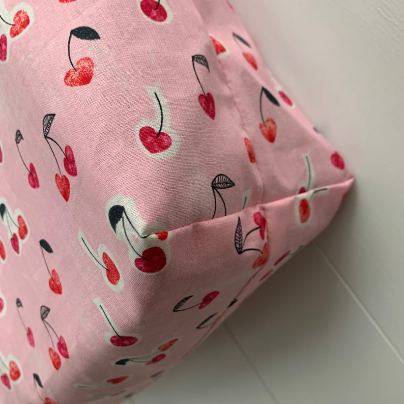 K&ouml;nnte beinhalten: Rosa Stofftasche mit Kirschendruck. Die Tasche ist gefaltet und die Naht ist sichtbar.