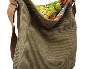 Può includere: Una borsa a tracolla in velluto a coste verde oliva con un'ampia tracolla in tessuto color cuoio e finiture color ottone. La fodera interna presenta un vivace motivo floreale nei toni del verde lime, rosa e viola, con chiusura magnetica.