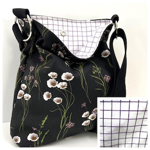 May include: Black shoulder bag with a floral pattern featuring white and brown flowers, green stems, and purple accents. The bag has a black strap and silver metal rings. The interior lining is white with a purple grid pattern.