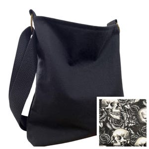 May include: A black crossbody bag with a wide fabric strap and metal rings. An inset square shows a detailed black and white pattern featuring multiple human skulls interspersed with blooming roses, providing a contrast to the solid black bag.