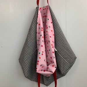 K&ouml;nnte beinhalten: Eine schwarze und wei&szlig;e Gingham-Tragetasche mit roten Griffen. Das Innere der Tasche ist mit einem rosa Stoff mit Kirschendruck ausgekleidet.