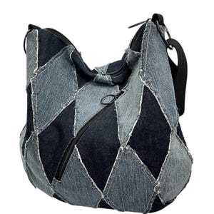 May include: A denim patchwork shoulder bag with a black zipper and strap. The bag is made of various shades of blue denim, stitched together in a geometric pattern. The bag has a black zipper and a black strap.