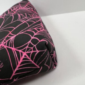 K&ouml;nnte beinhalten: Eine schwarze und pinkfarbene Stofftasche mit einem Spinnennetz-Muster. Die Tasche ist aus einem weichen, strapazierf&auml;higen Material gefertigt und hat einen Rei&szlig;verschluss.