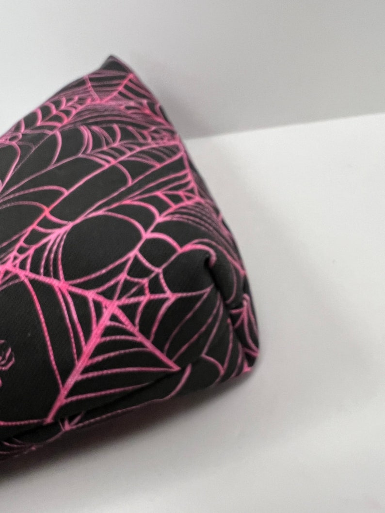 K&ouml;nnte beinhalten: Eine schwarze und pinkfarbene Stofftasche mit einem Spinnennetz-Muster. Die Tasche ist aus einem weichen, strapazierf&auml;higen Material gefertigt und hat einen Rei&szlig;verschluss.