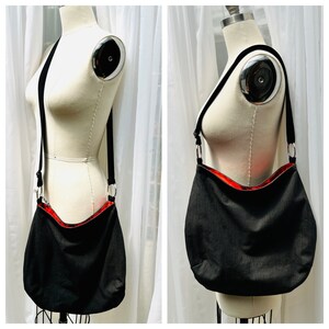 May include: Black corduroy shoulder bag with a red interior. The bag has a long black strap and silver-colored metal rings. The bag is displayed on a mannequin against a white curtain backdrop.