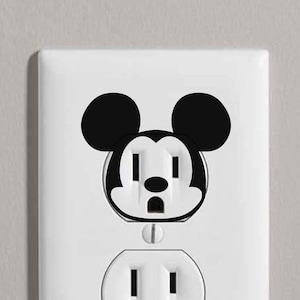 May include: A white electrical outlet cover with a black Mickey Mouse face sticker on it.