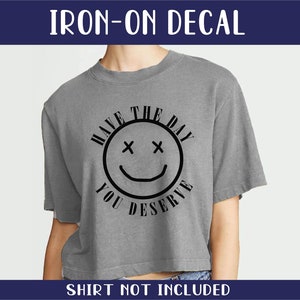 Puede incluir: Calcomanía de planchado con una cara sonriente y el texto "Have the day you deserve".