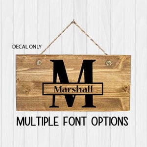 May include: Wooden sign with a black letter "M" and the name "Marshall" printed below. The sign is hanging from a rope and has a rustic look. "Decal Only" and "Multiple Font Options" are printed below the sign.