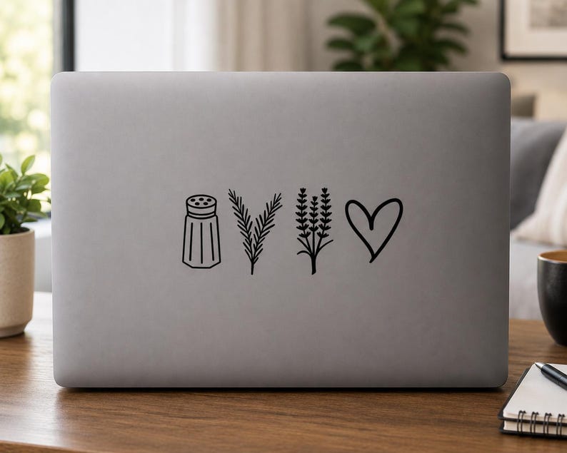 Op de afbeelding: Een matgrijze laptopdeksel met een zwarte vinylsticker. Het ontwerp bestaat uit vier afzonderlijke iconen die horizontaal zijn gerangschikt: een zoutvaatje, een takje rozemarijn, een lavendeltak en een handgetekende hartvorm.