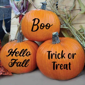 May include: Three orange pumpkins stacked together, each with a dark green stem. The top pumpkin has the word "Boo" written on it. The bottom left pumpkin says "Hello Fall", and the bottom right pumpkin says "Trick or Treat".
