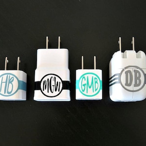 May include: Five white wall phone chargers with personalized monogram stickers. The stickers are black, gray, and teal with white letters. The monograms are "HB", "MGW", "GMB", and "DB".