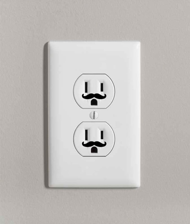 May include: A white electrical outlet with two outlets, each with a black mustache sticker above the slots.