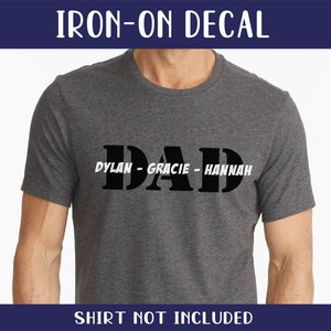 May include: Iron-on decal with the word "DAD" in large black letters and the names "DYLAN", "GRACIE", and "HANNAH" in smaller white letters below.  The decal is on a gray t-shirt.