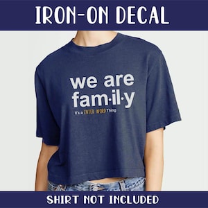以下が含まれることがあります： 紺色のTシャツに白い文字で「we are fam-il-y」と書かれたアイロン接着の転写シート。メインテキストの下に黄色で「It's a ENTER WORD Thing」と書いてあります。