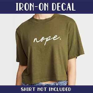 May include: Iron-on decal with the word "nope" written in white cursive on a green t-shirt.  Shirt not included.