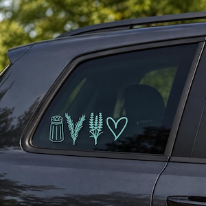Op de afbeelding: Een lichtblauwe vinylsticker op een donkergrijze autoruit, met vier lijntekeningen: een zoutvaatje, een takje rozemarijn, een lavendeltak en een eenvoudige hartvorm, allemaal in een horizontale rij naast elkaar geplaatst.