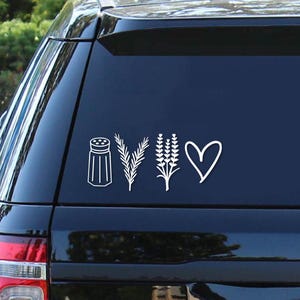 May include: A white vinyl sticker featuring a salt shaker, two sprigs of rosemary, a bunch of lavender, and a heart. The sticker is applied to the rear window of a black car.