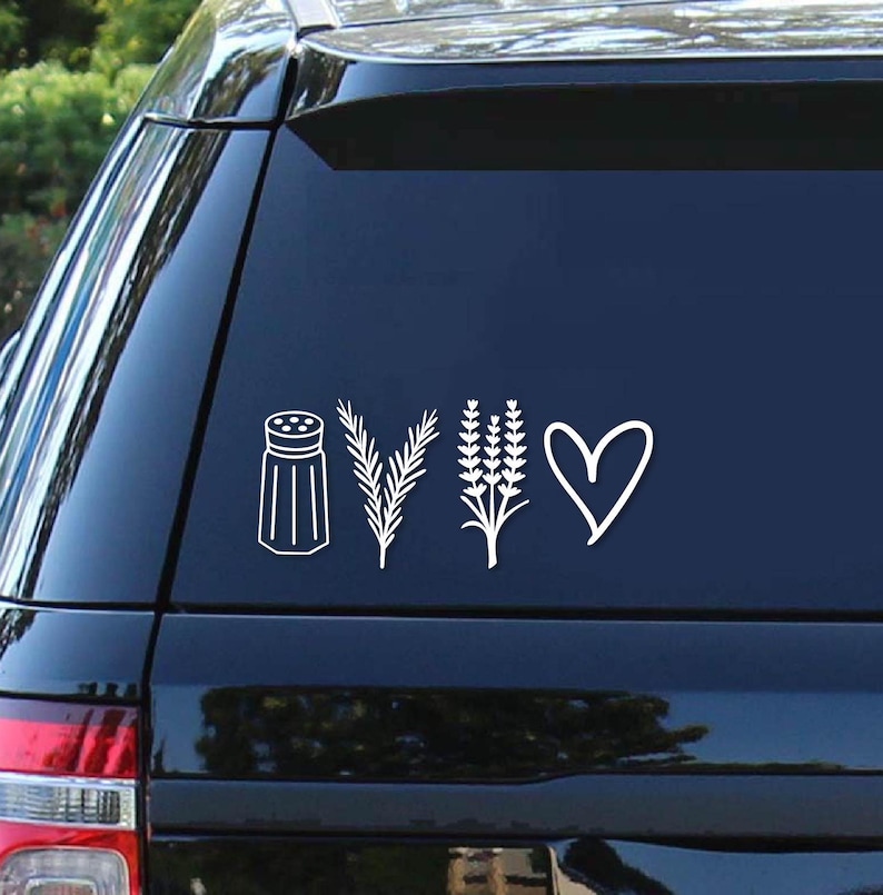 May include: A white vinyl sticker with a salt shaker, two sprigs of rosemary, a bunch of lavender, and a heart. The sticker is on the back window of a black car.