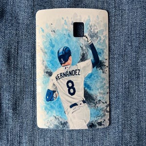 May include: A rectangular, white key fob featuring a watercolor painting of a baseball player in a white uniform with the name "Hernandez" and the number "8" on the back. The background has blue watercolor splashes.