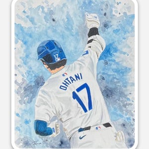 May include: Watercolor sticker featuring a baseball player in a white uniform with the number 17 and the name "Ohtani" on the back. The player is celebrating with his arm raised against a blue watercolor background.