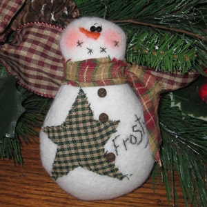 May include: A white snowman ornament with a red and green plaid scarf, a brown star, and the word "Frost" embroidered on the front.