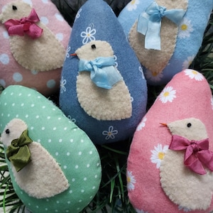 May include: Five felt Easter eggs decorated with birds and bows. The eggs are pink, blue, green, and white with polka dots and floral patterns.