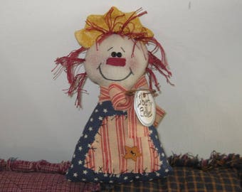 May include: A handmade rag doll with red hair, a yellow hat, and a red, white, and blue striped dress. The doll is holding a tag that says "Liberty Belle".